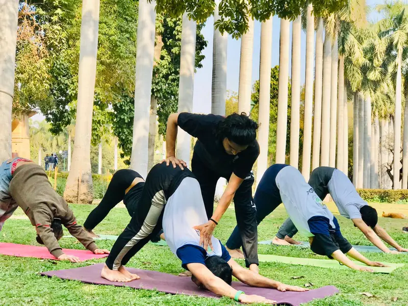 The teacher adjusting a student's back in downward dog during an outdoor group class